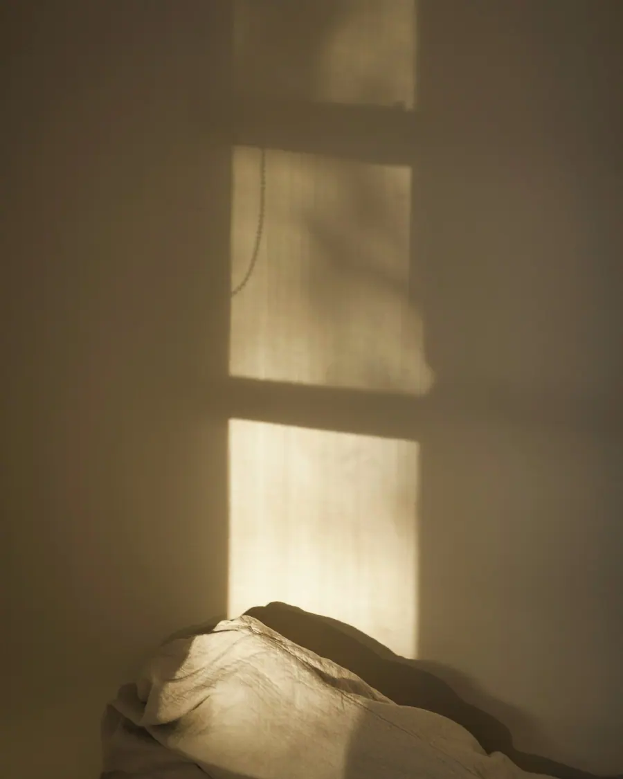 Luz de uma janela desenhada na parede sobre a roupa de cama.